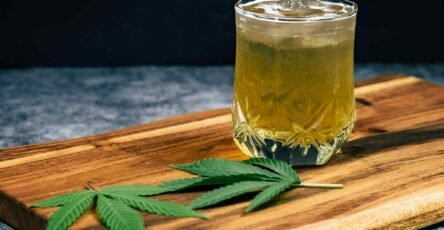 Image of of Delta-9 THC drink in a glass on the table, near some hemp leaves.