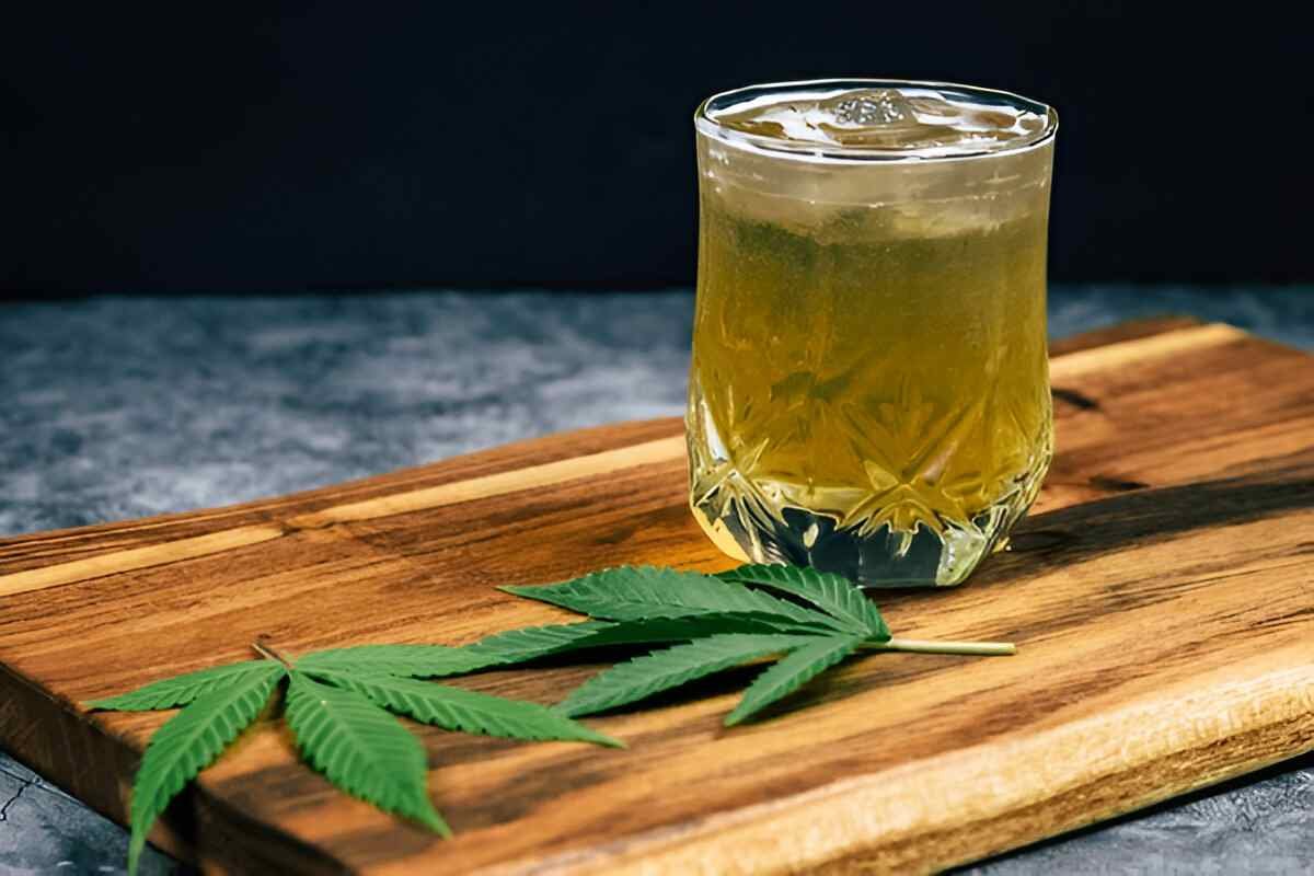 Image of of Delta-9 THC drink in a glass on the table, near some hemp leaves.